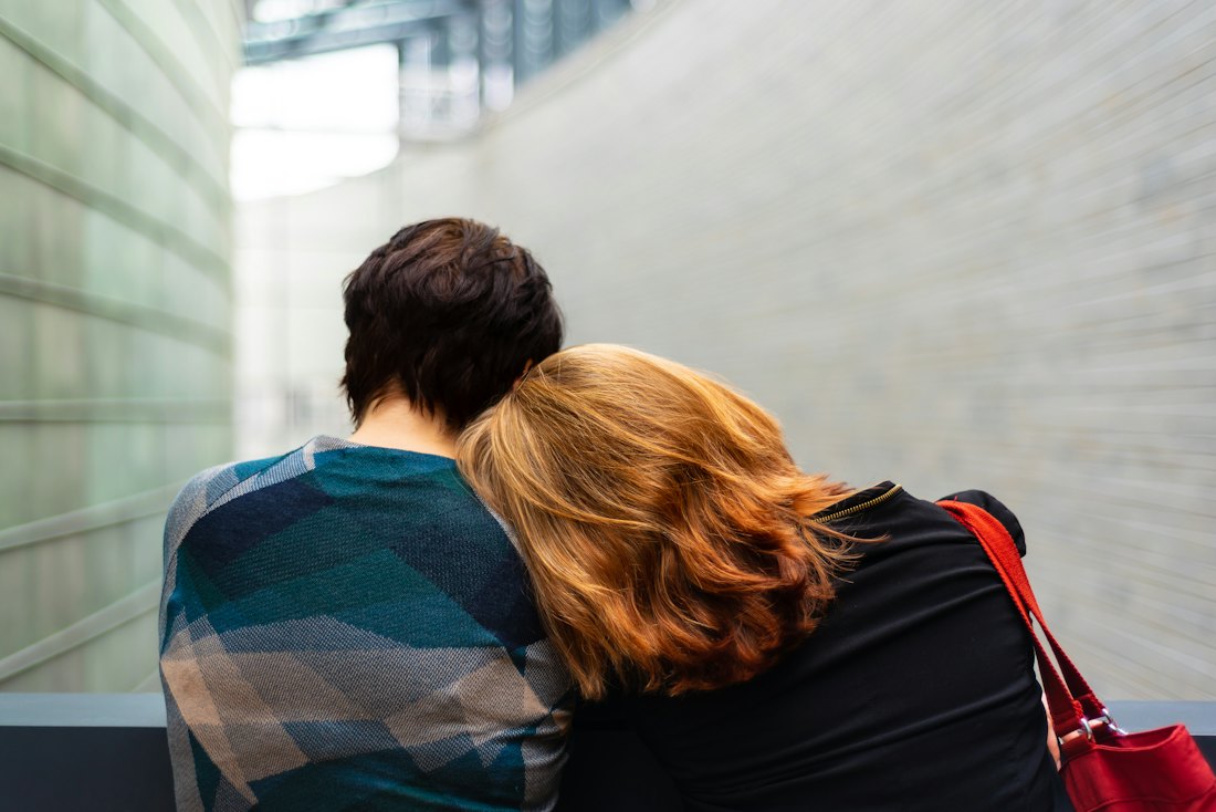 Two people sitting close, one leaning on the other for support