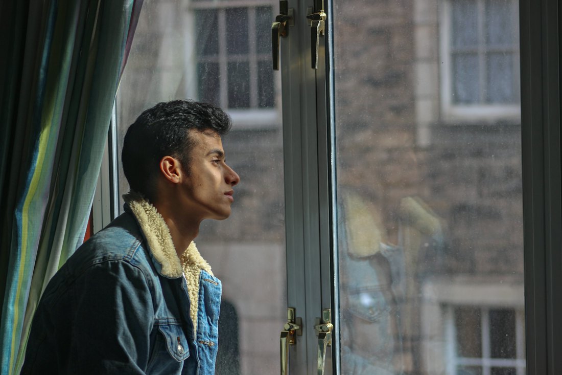 A man looking out a rain-streaked window, lost in thought