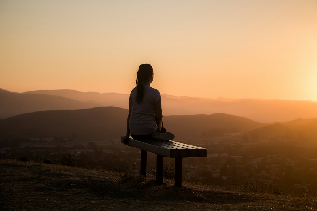 A person on a hilltop bench watching the sunrise