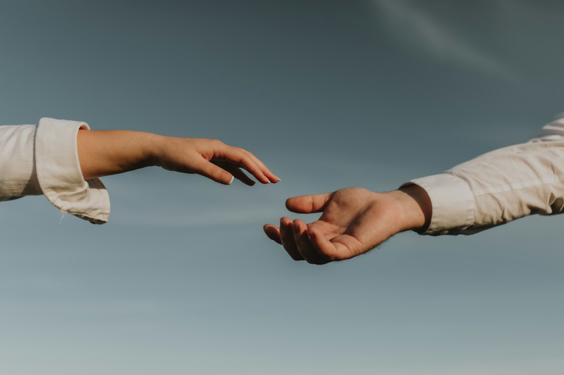 Two hands reaching toward each other against an open sky